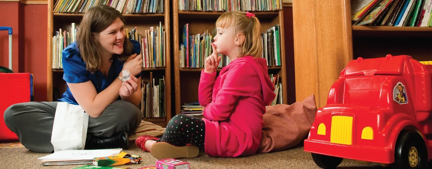 Speech language therapist conducting assessment with child in a playroom.